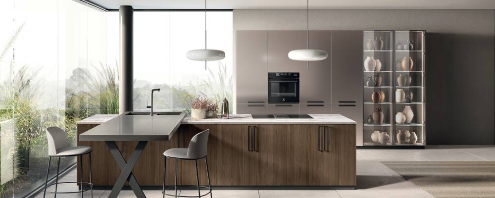 Kompozisyon, antrasit kaplama metalden dikey kulplarla donatılmış Pecan Meşe çıta kaplamalı kapılı bir ada ile övünüyor; Invisible Light Porcelain Stoneware üst, 2 cm kalınlığında 6G60 profil ve yıkama alanı olan Dark Steel üst, 6 cm kalınlığında 2J profil ile birleşiyor. Pas Dosé sedefli mat lake kapılı, antrasit kaplama metalden yatay kulplarla donatılmış uzun kiler üniteleri ve uzun cihaz üniteleri; sağda Dark Steel çerçeveli ve şeffaf Stopsol cam kapılı uzun üniteler.